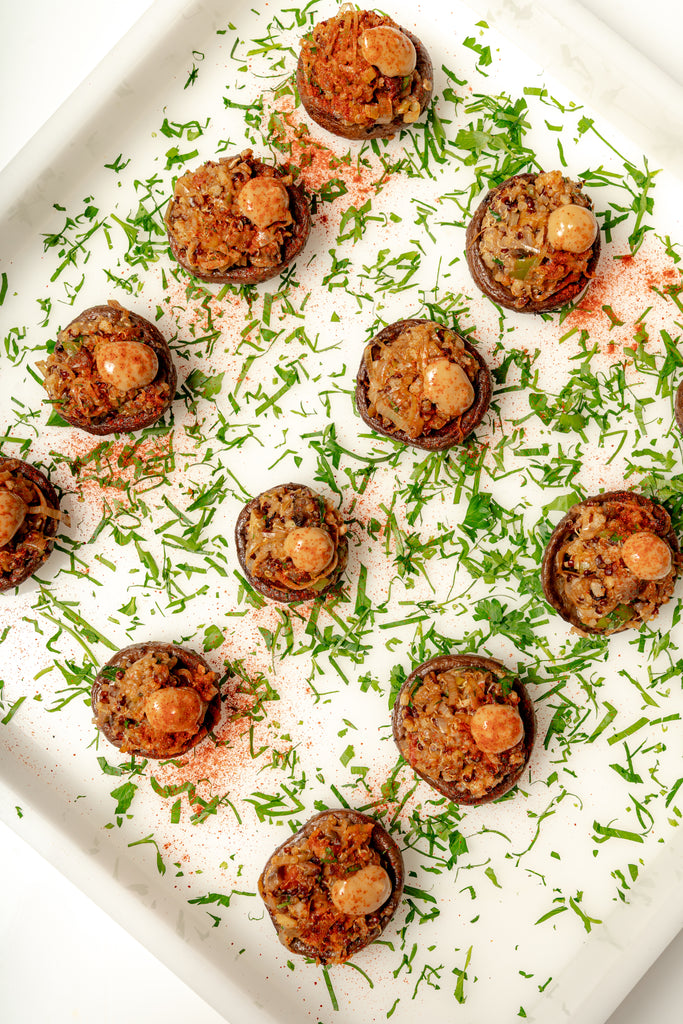 Mini Tuscan Stuffed Mushrooms arranged on a white tray, garnished with chopped herbs and paprika, served alongside a balsamic aioli.