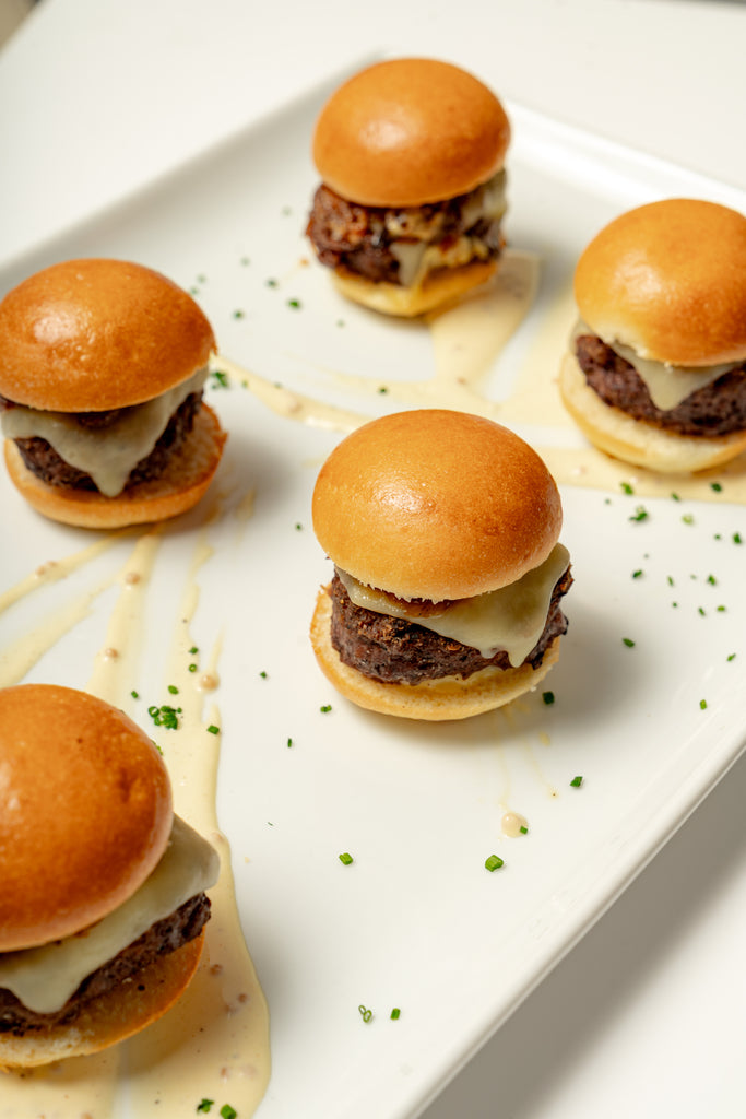 Wagyu Mini Burgers: Five mini wagyu burgers with melted aged white cheddar, light creamy sauce, and chopped chives, served on mini brioche buns.