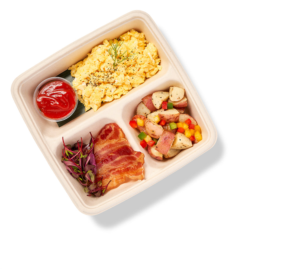 A Breakfast Bento Box with eggs, bacon, and ketchup, containing a meat entree.