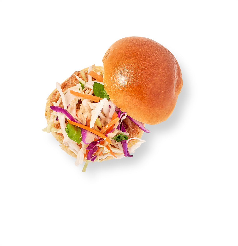 Description: A BBQ Pulled Chicken on Brioche slaw sandwich drizzled with homemade barbecue sauce on a white background.