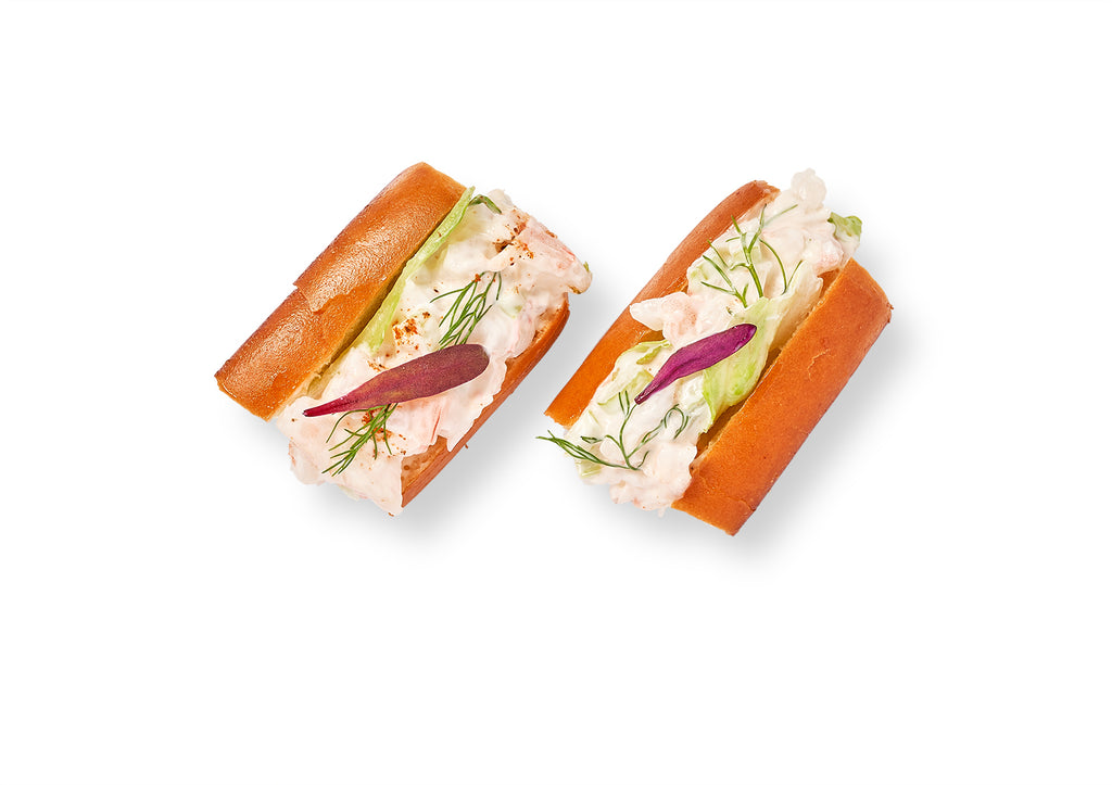 Two lobster salad on mini roll with salmon and dill on a white background, served on miniature buttered brioche rolls.