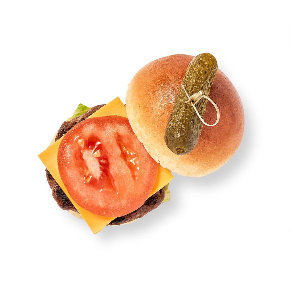 A Mini Hamburger on Brioche with tomato and pickle topped with ketchup on a white background.