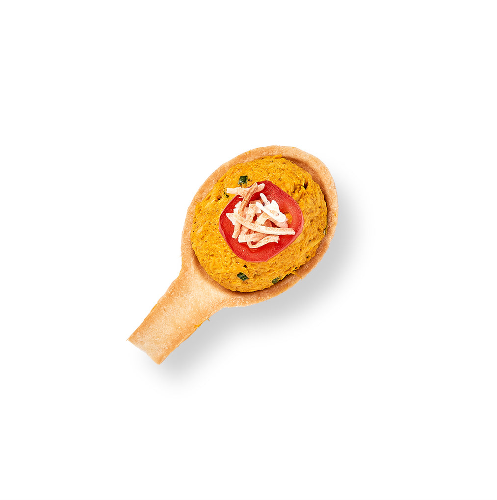 An edible spoon filled with Moroccan Chicken Salad and topped with coconut flakes, placed on a white background.