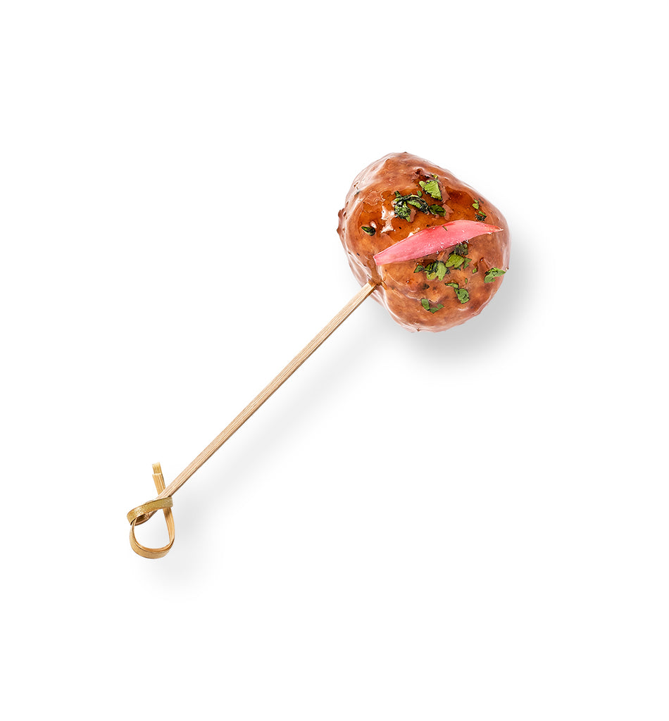 A lollipop stick with Homemade Swedish Meatballs served on it, drizzled with tangy sauce.