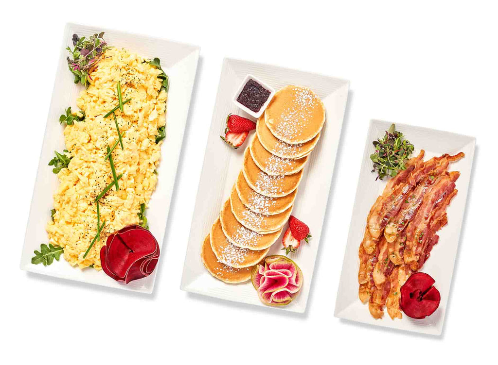 Three New York Breakfast Packages with scrambled eggs, pancakes, and bacon on them.