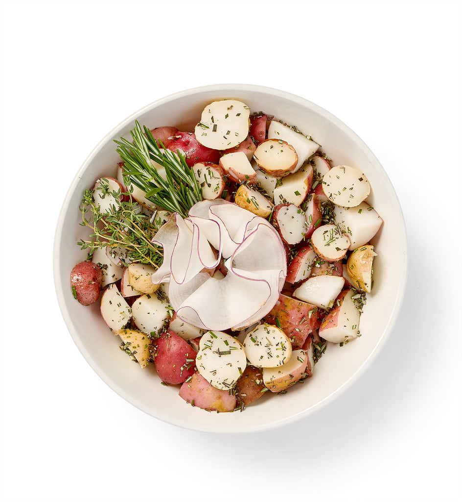 A white bowl filled with roasted rosemary red potatoes and sprigs of rosemary.