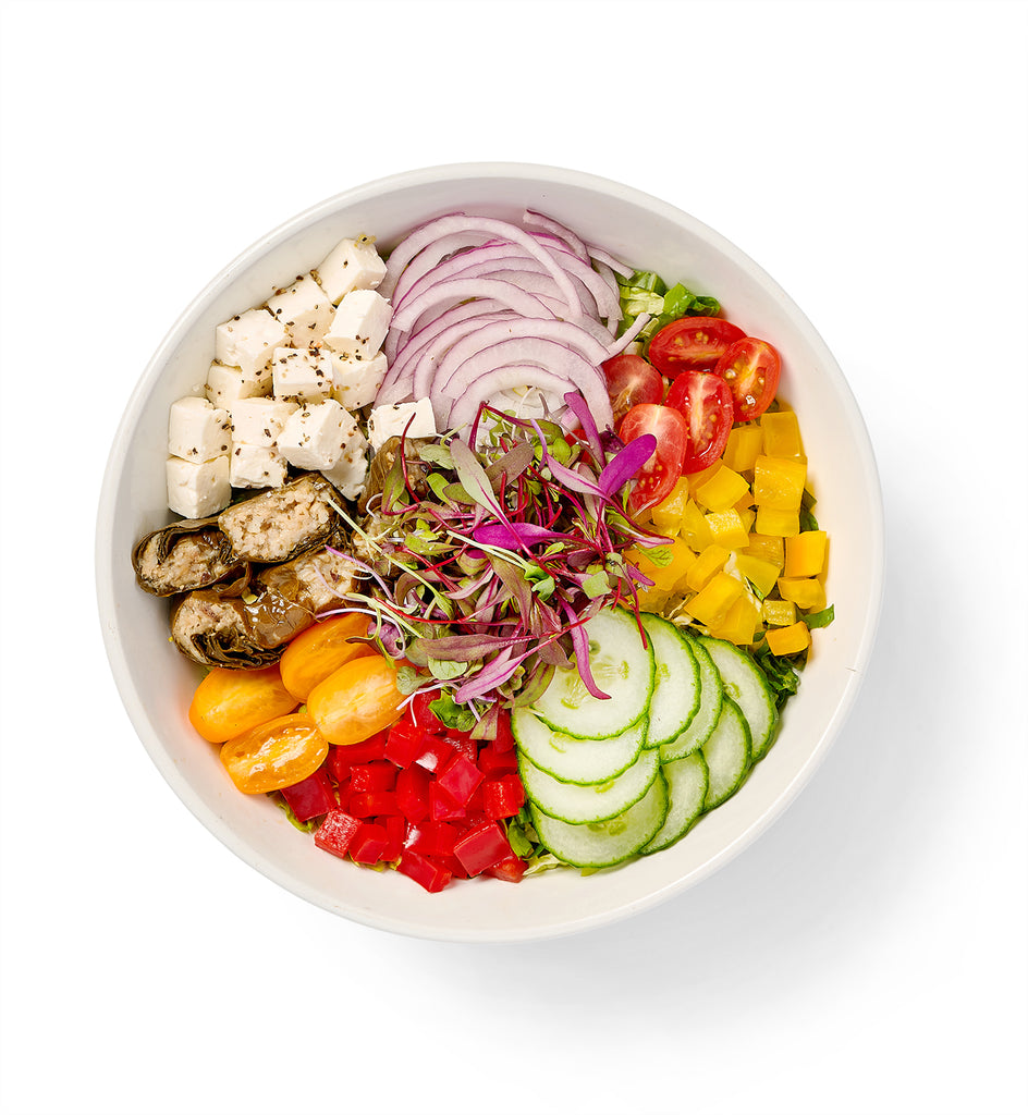 A white bowl filled with a Greek Salad including feta cheese and tomatoes.