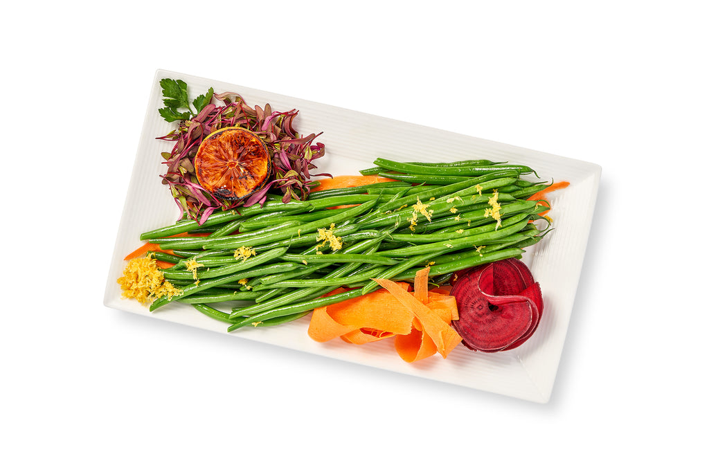A white plate with sautéed string beans, carrots and beets topped with a hint of lemon zest.