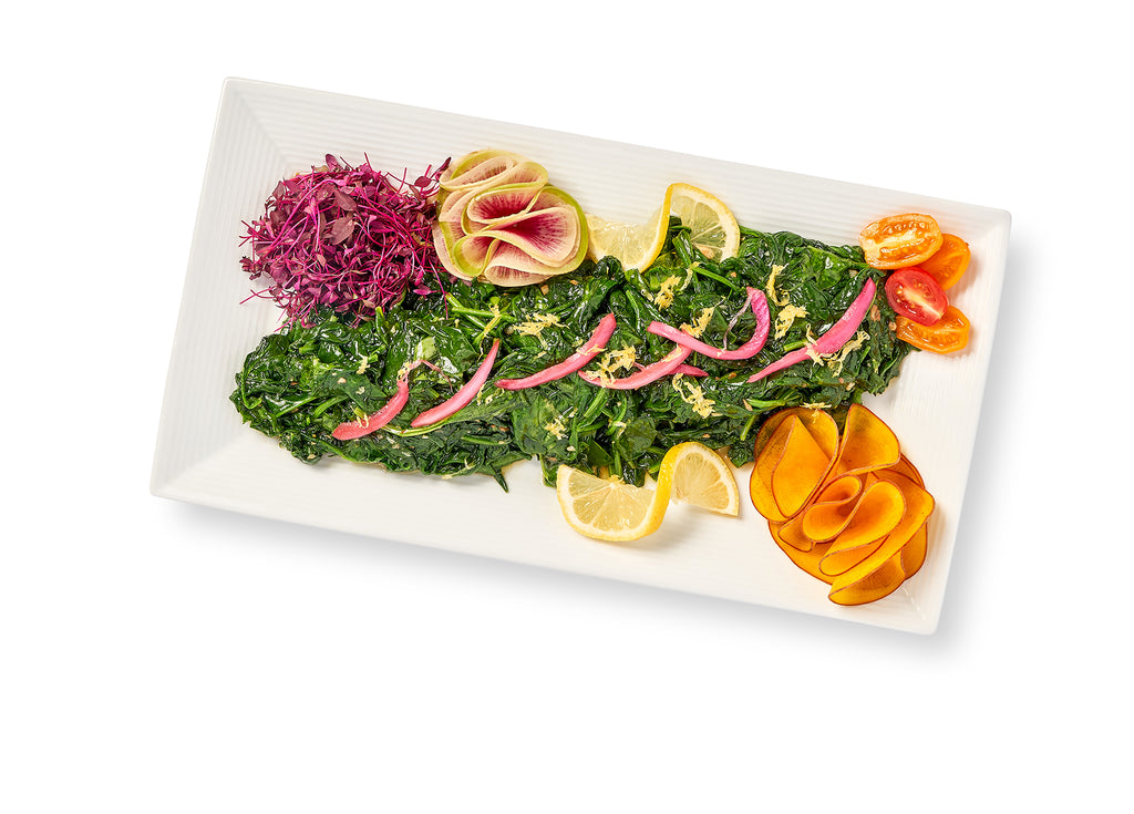 A plate with blanched spinach, carrots and lemons drizzled with extra virgin olive oil.